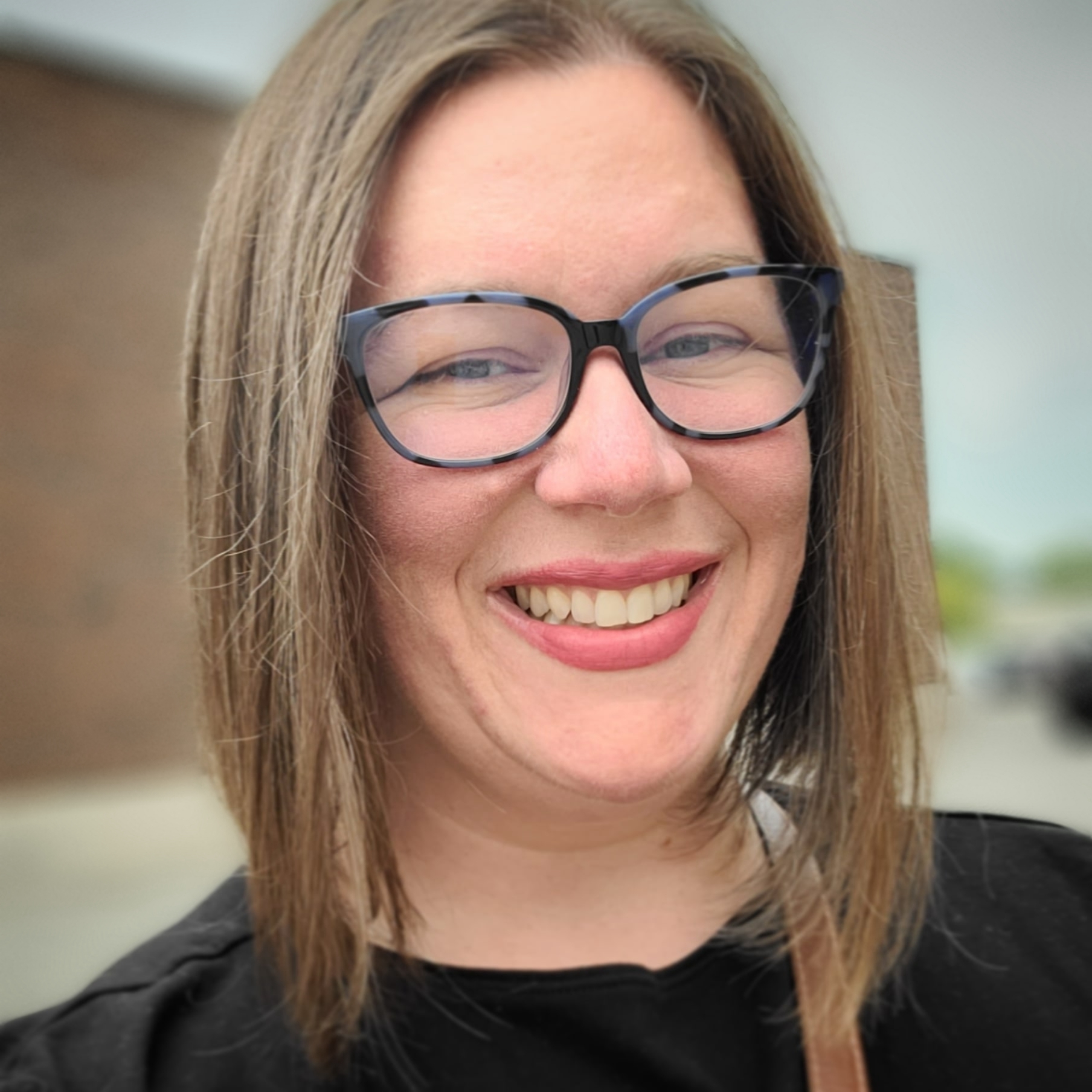 Portrait of Julia Sperry, smiling, with a long bob haircut and glasses.
